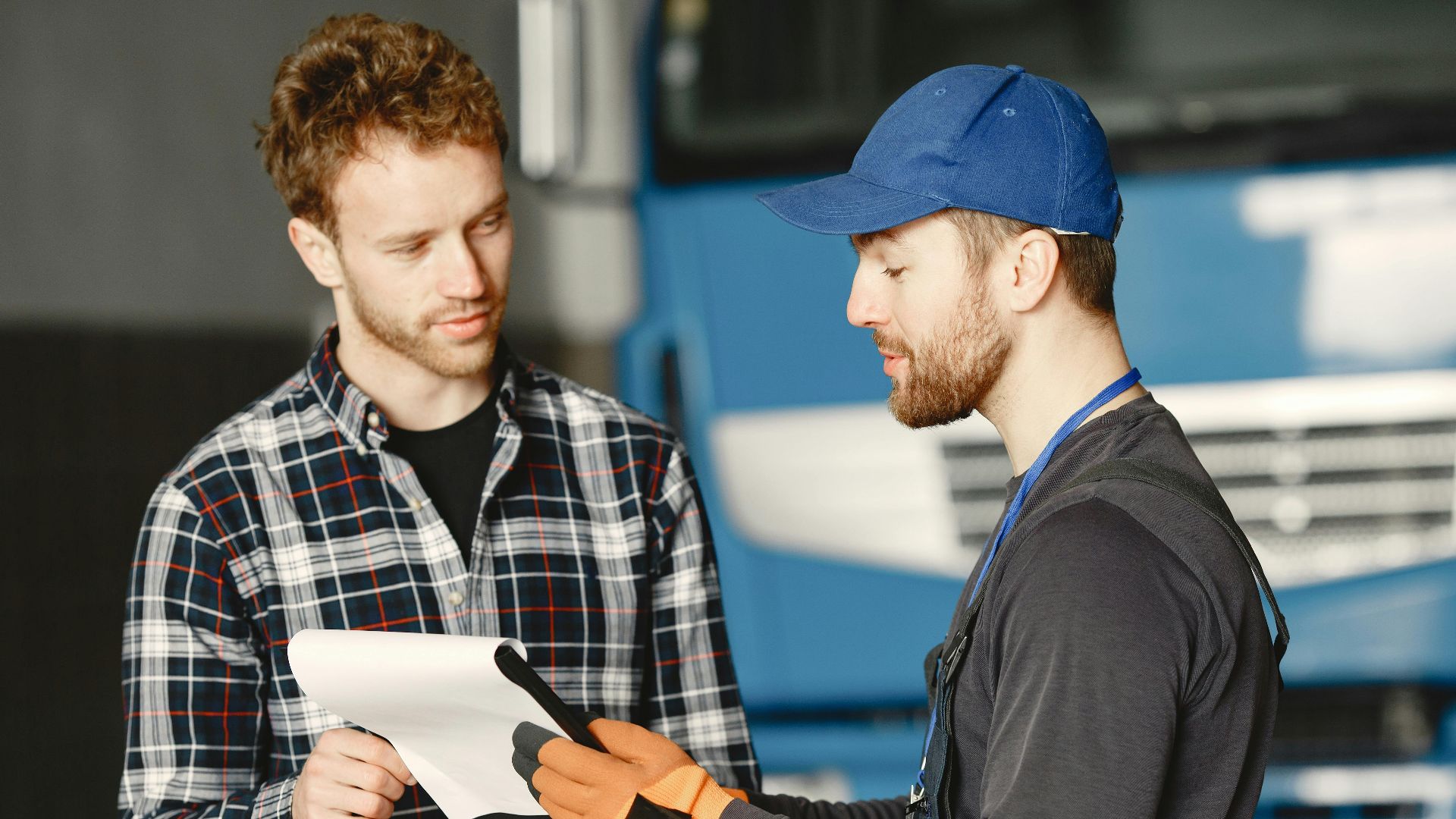 Mechanic in uniform talks with a customer about vehicle maintenance inside a garage.
