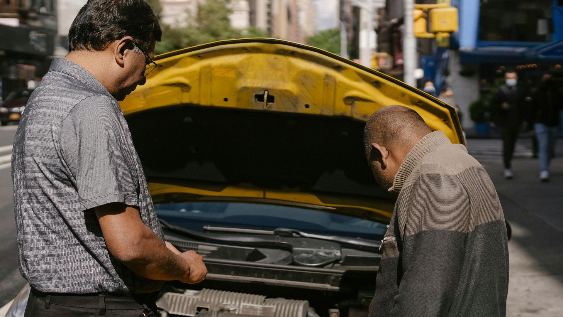 Back view of ethnic man identifying problems in engine system of car under hood standing near driver