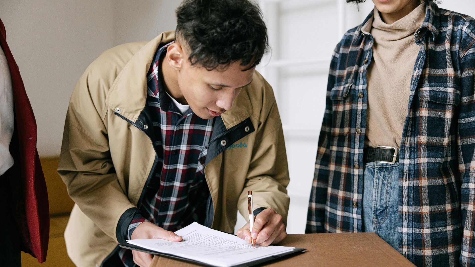 Young adults signing documents on moving day, finalizing new home purchase.