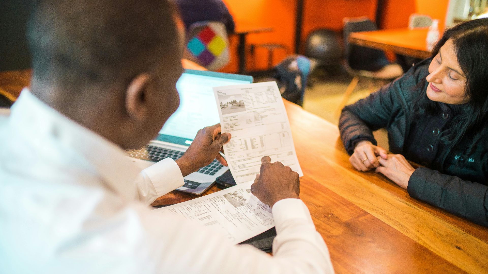 Two adults discussing documents in a business setting indoors.
