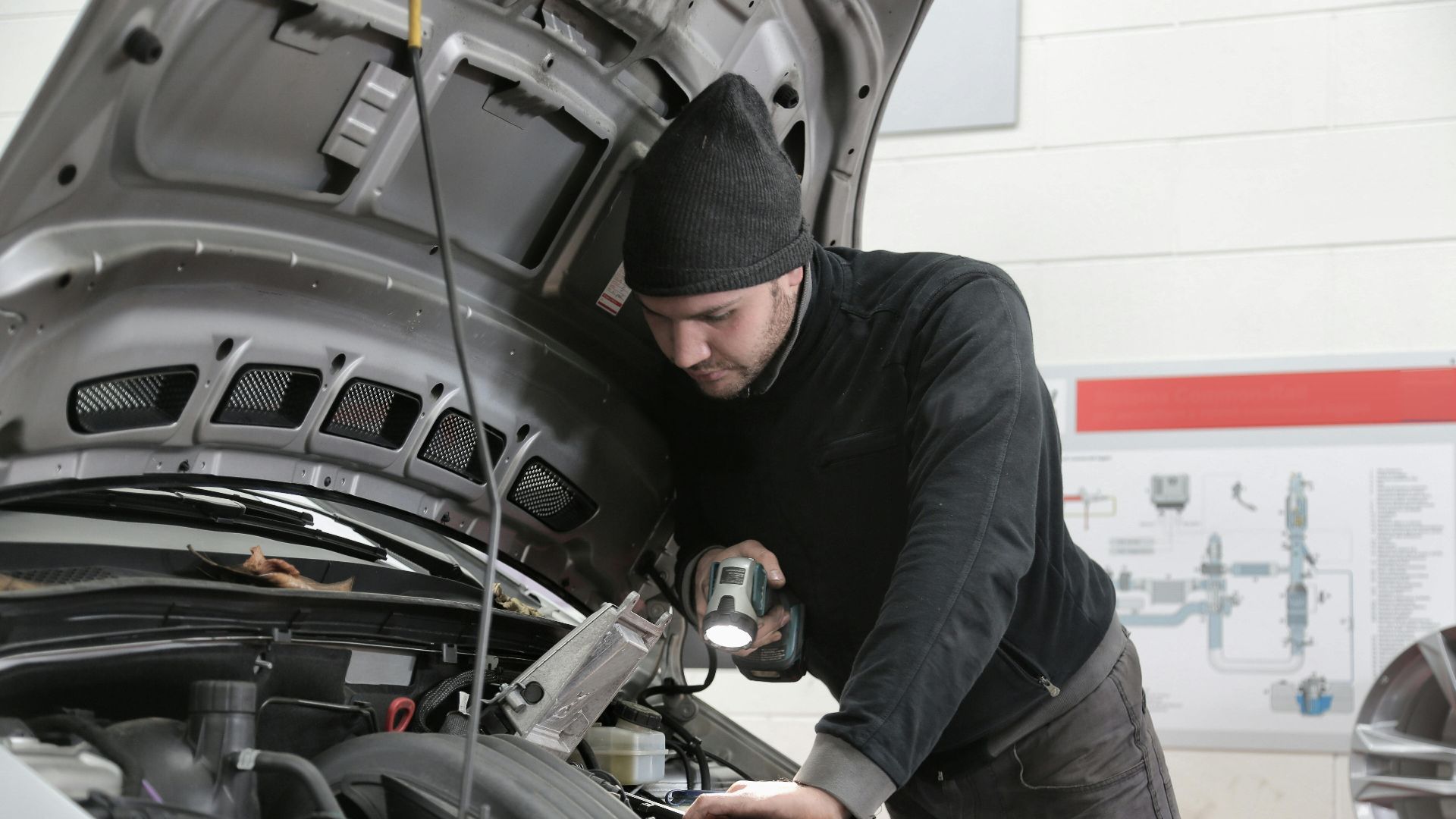 A mechanic closely inspects a car engine in a garage using a flashlight, ensuring proper maintenance.