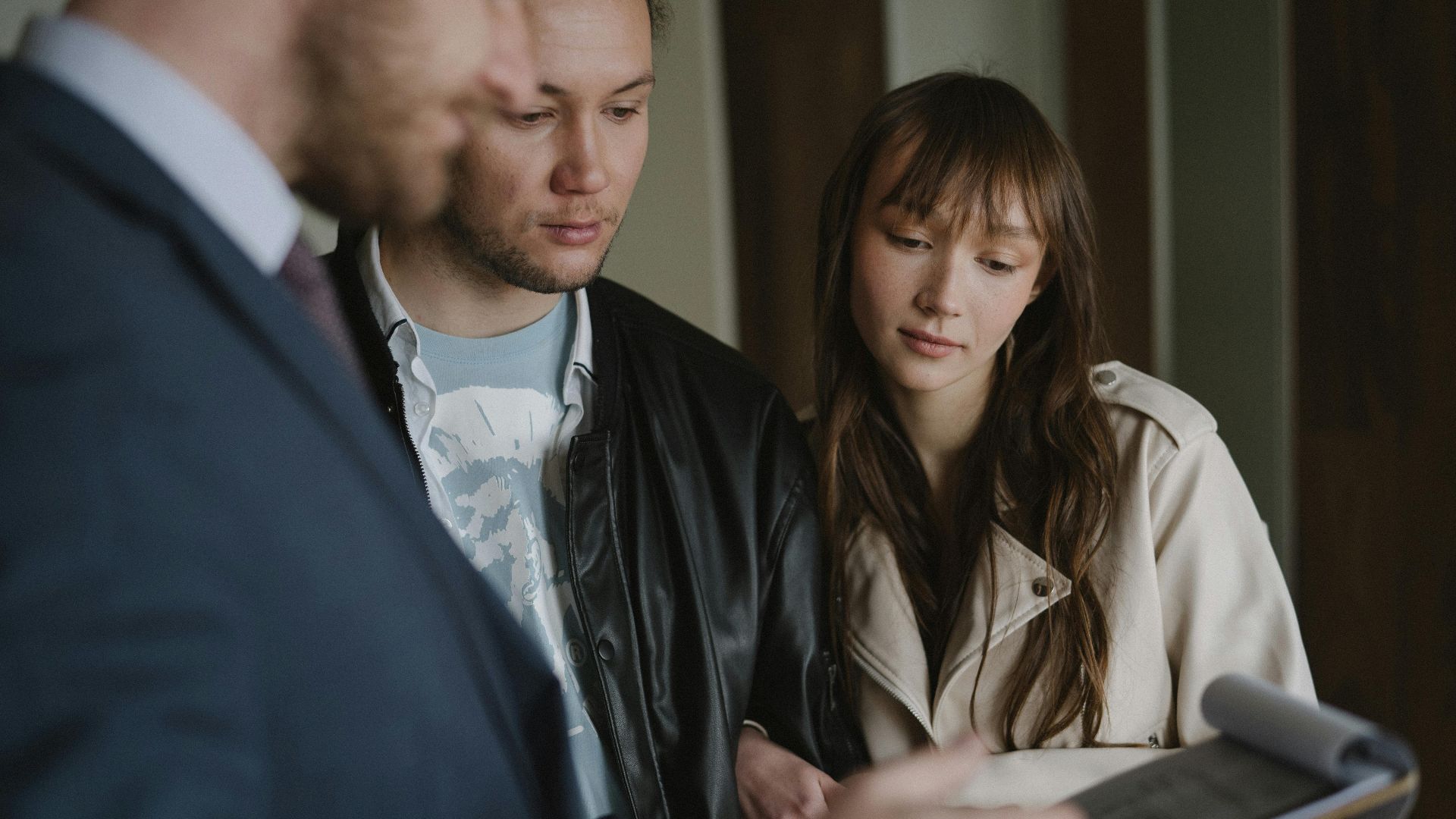 A couple discusses home buying details with a realtor inside a modern apartment.