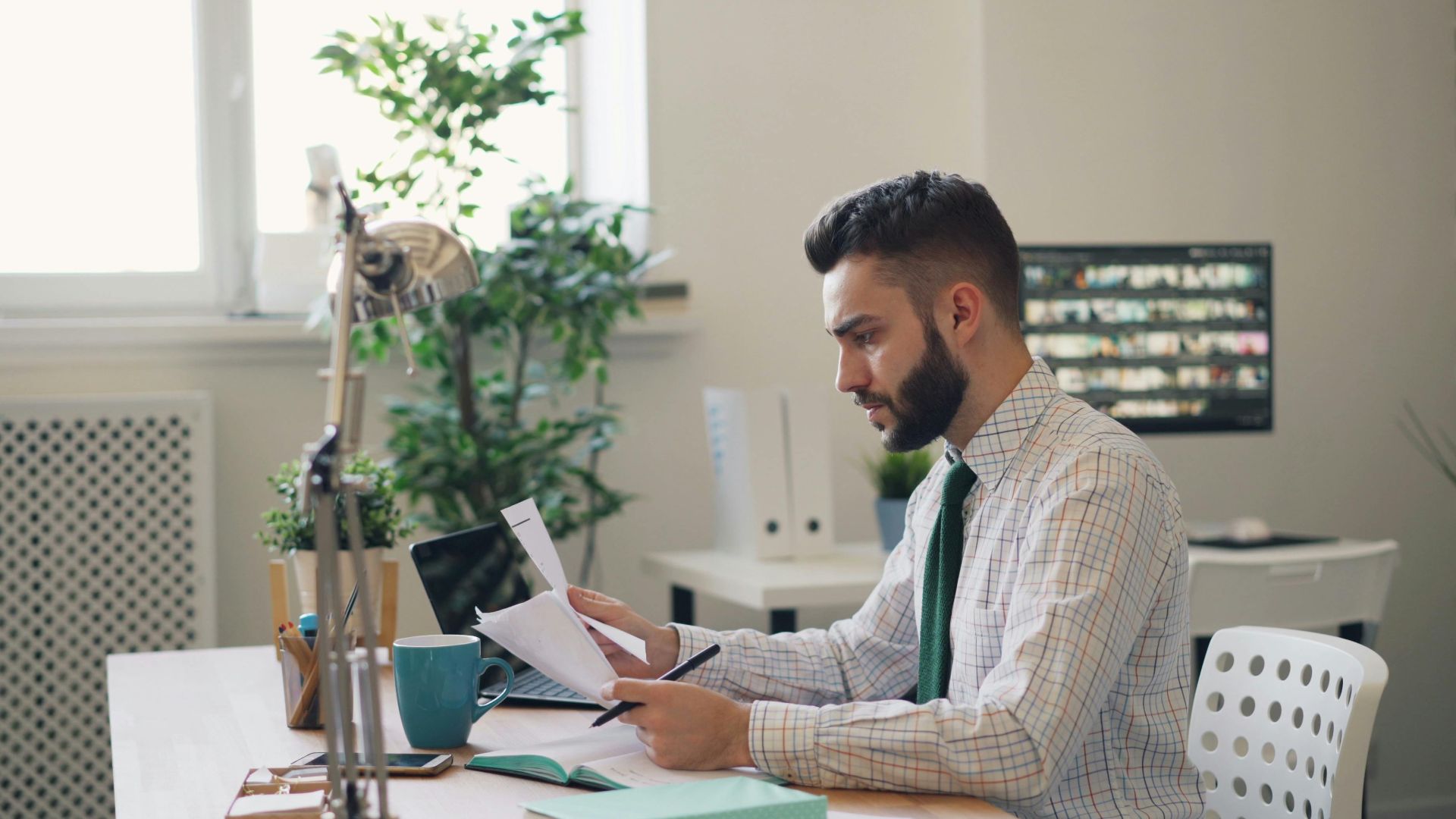 Focused man reviewing documents at a modern office desk with plants.