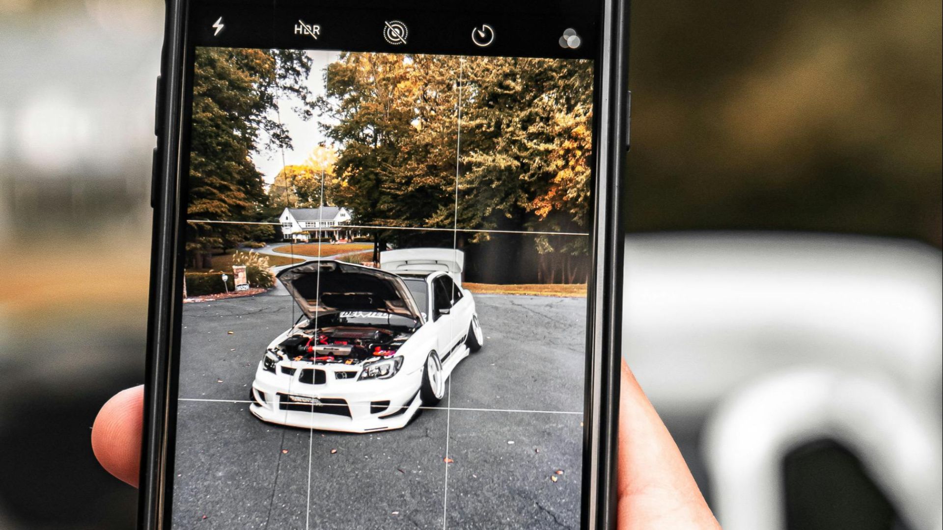 Person photographing a white car outdoors with a smartphone, showing technology and leisure.