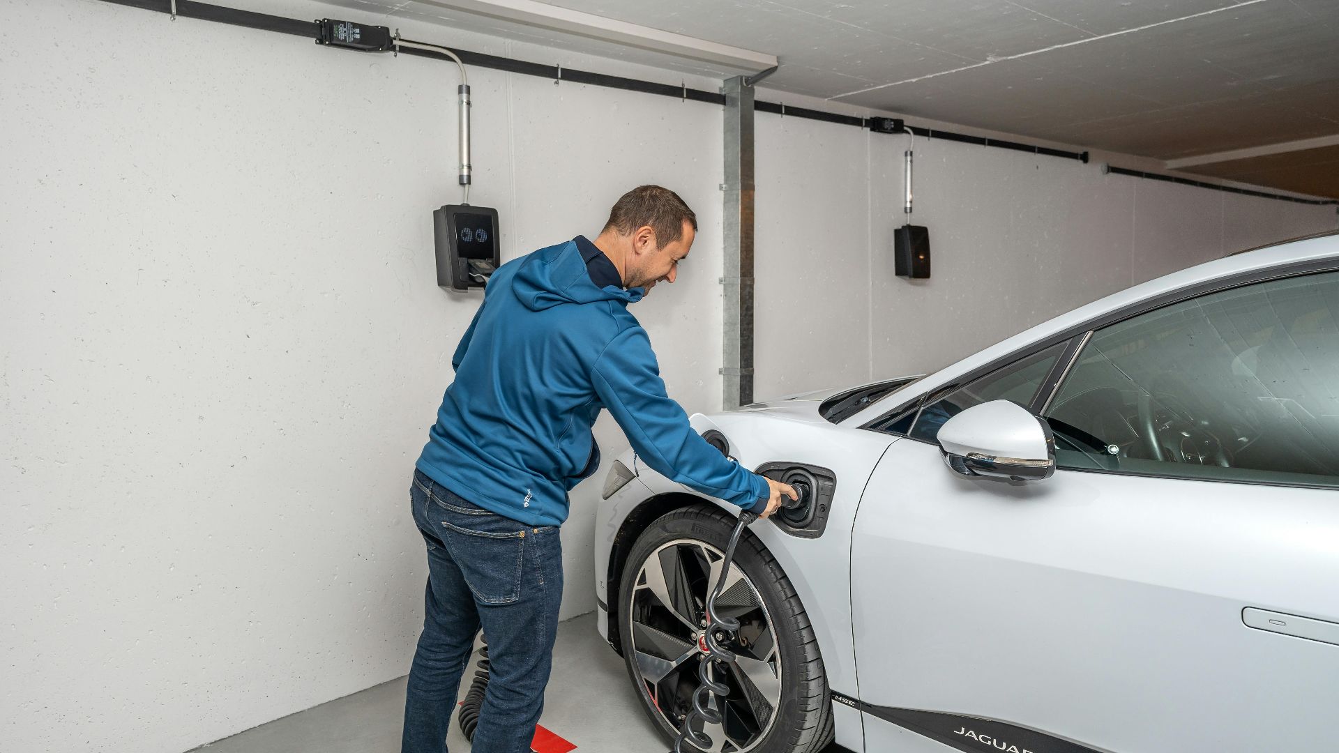 A man connects an electric car to a charging station in a modern indoor garage setting.