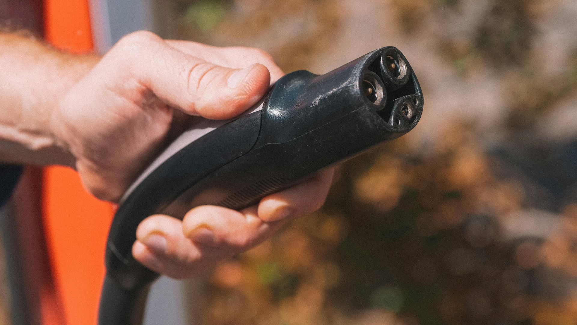Hand holding an electric vehicle charging plug, symbolizing clean energy and innovation.