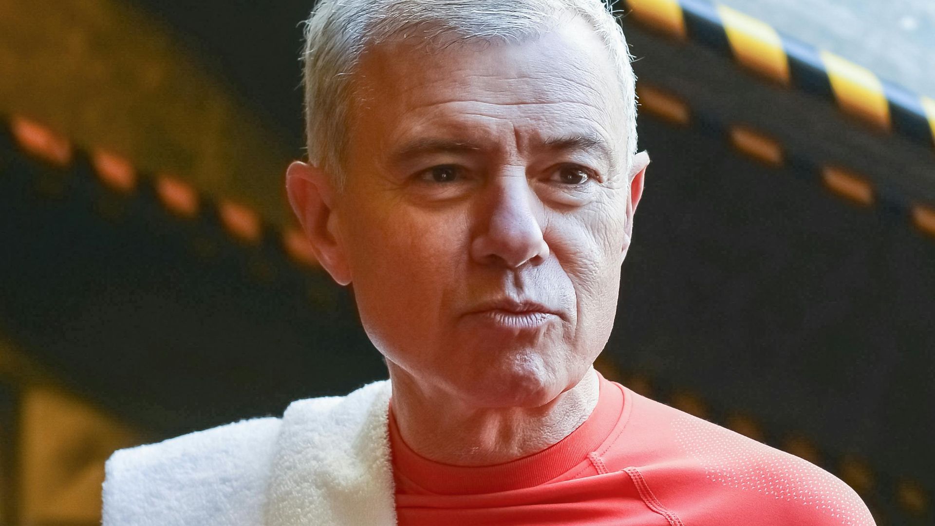 Elderly man in a red shirt with towel and water bottle during a gym break in Portugal.