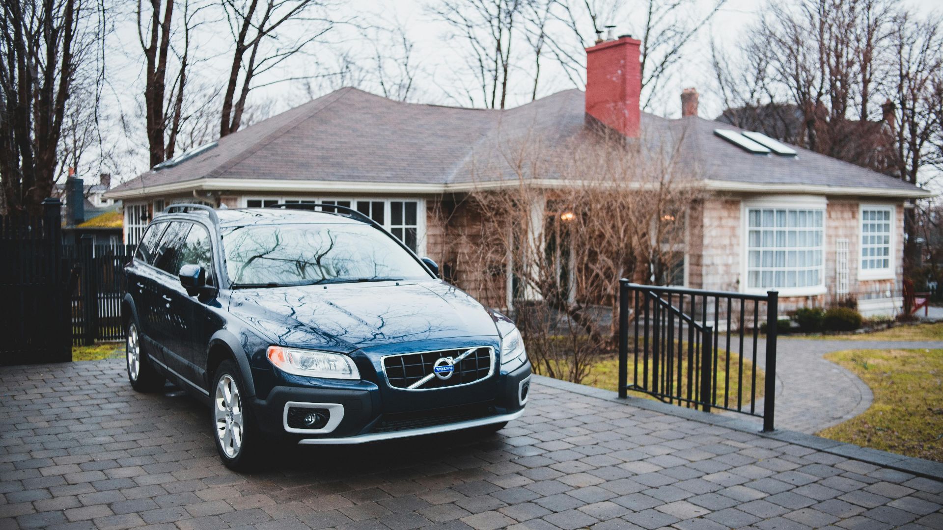 Exterior of new dark blue car placed near brick cottage surrounded by trees in cloudy day