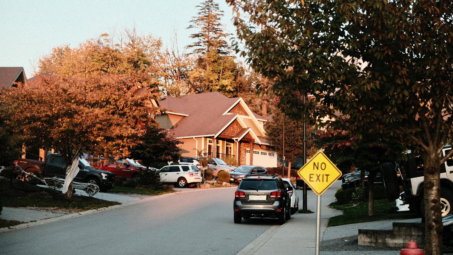 Charming suburban street scene with houses, cars, and a no exit sign in fall.