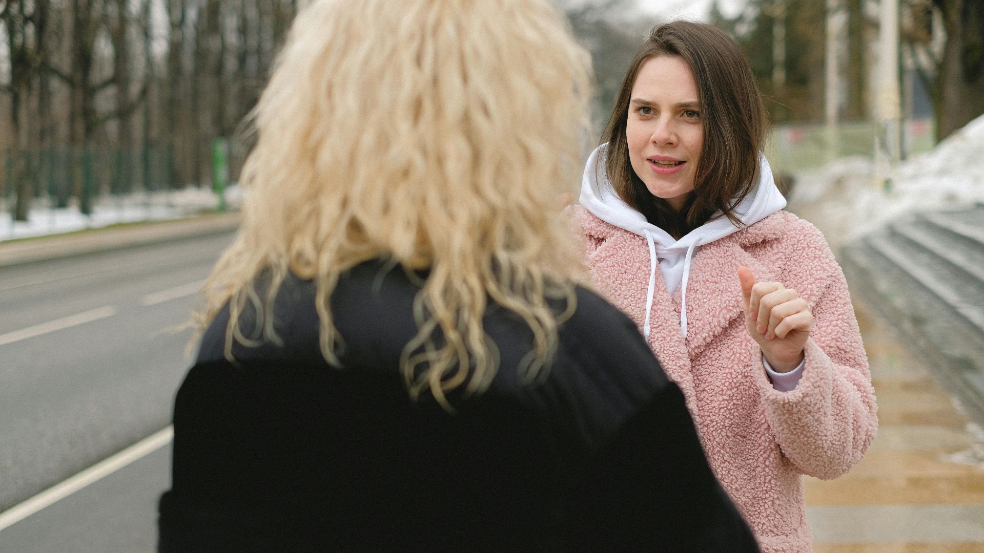 Back view of blond lady in warm clothes standing on street and having conversation with female friend in winter