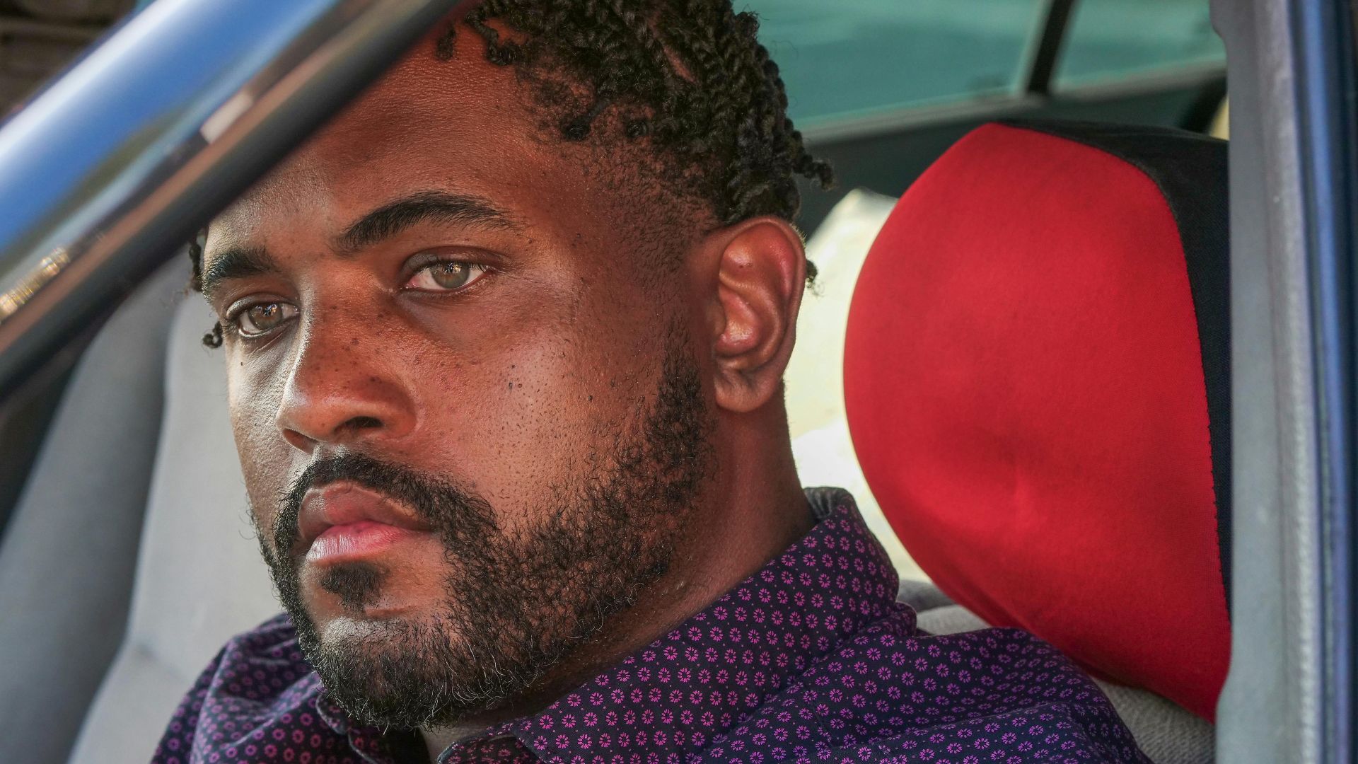 Close-up portrait of a man with facial hair sitting in a car staring intently.