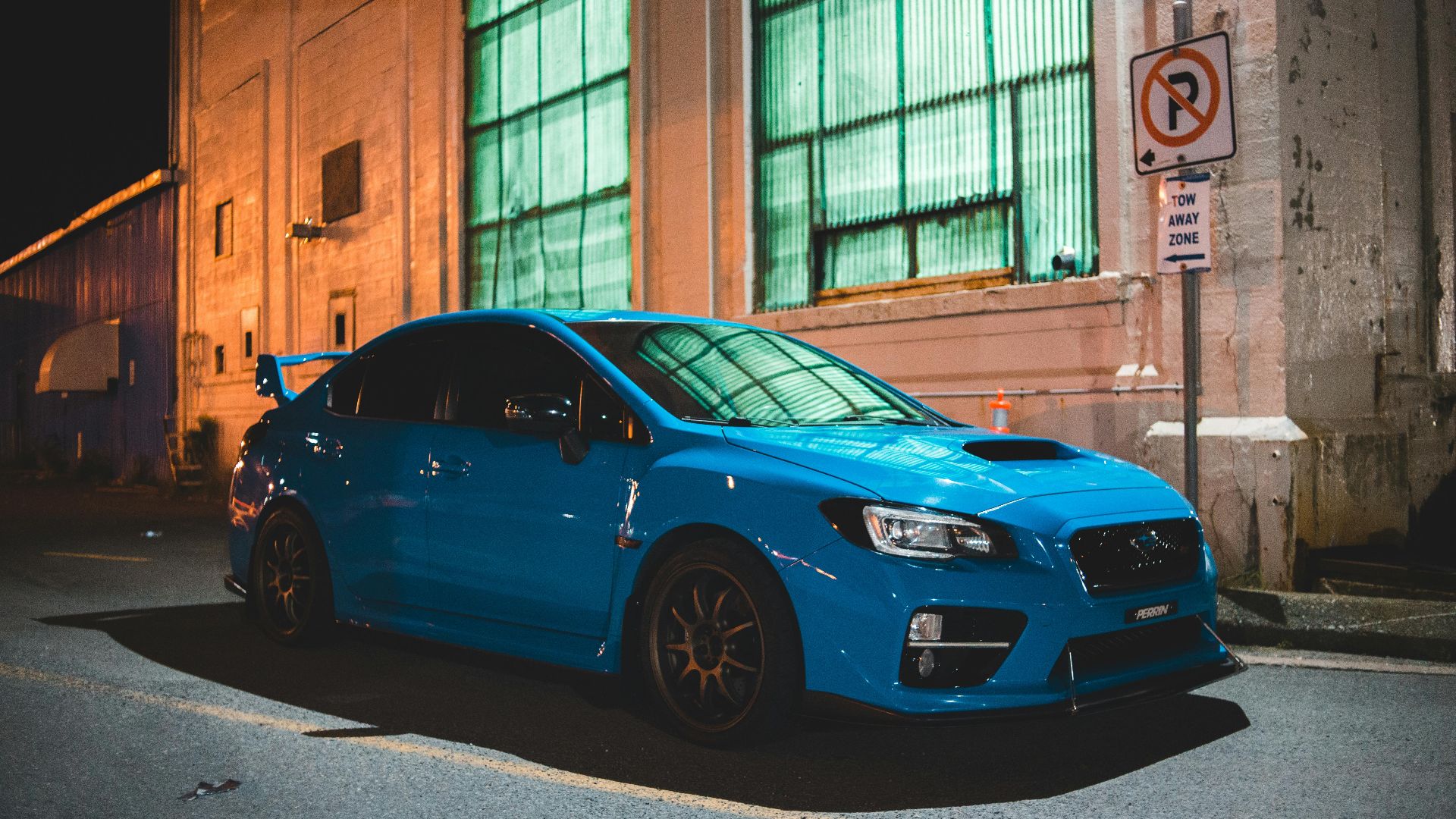 Contemporary blue automobile parked near aged weathered building with large windows in late evening
