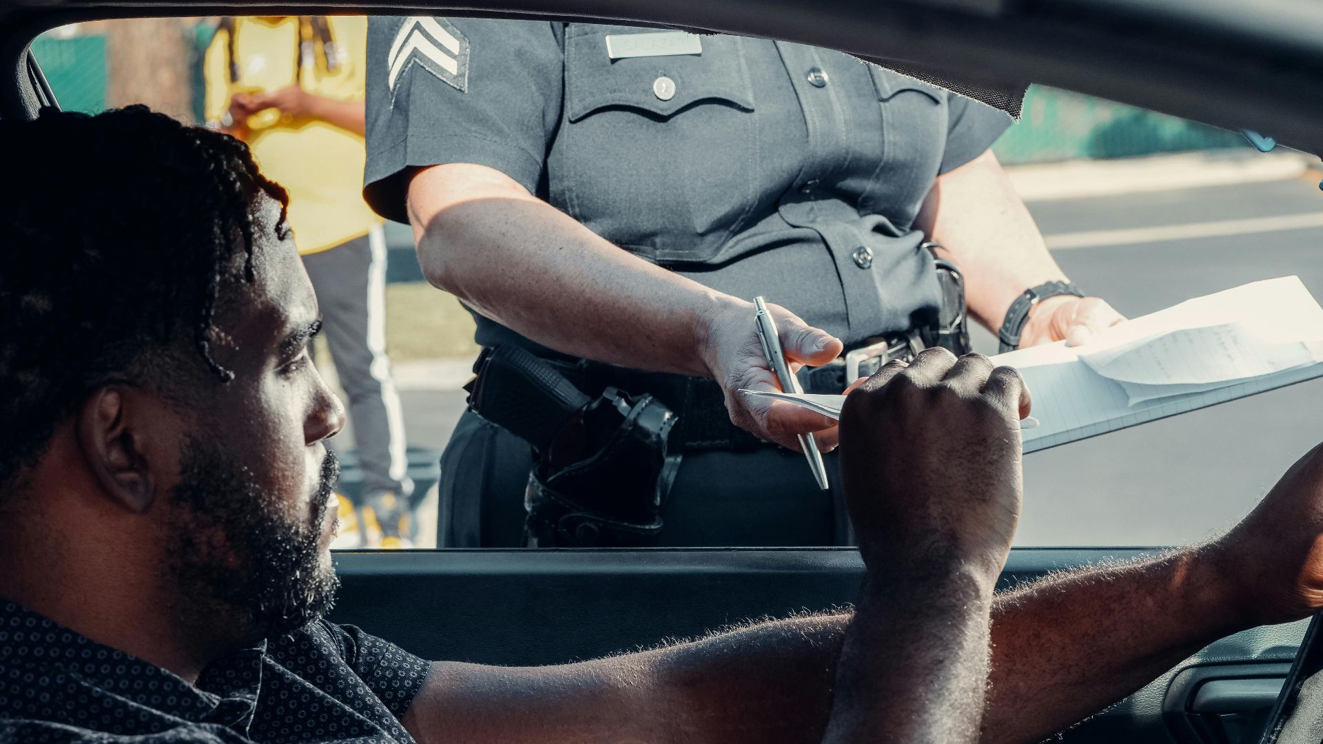 Police officer handing a traffic ticket to a driver during roadside inspection.