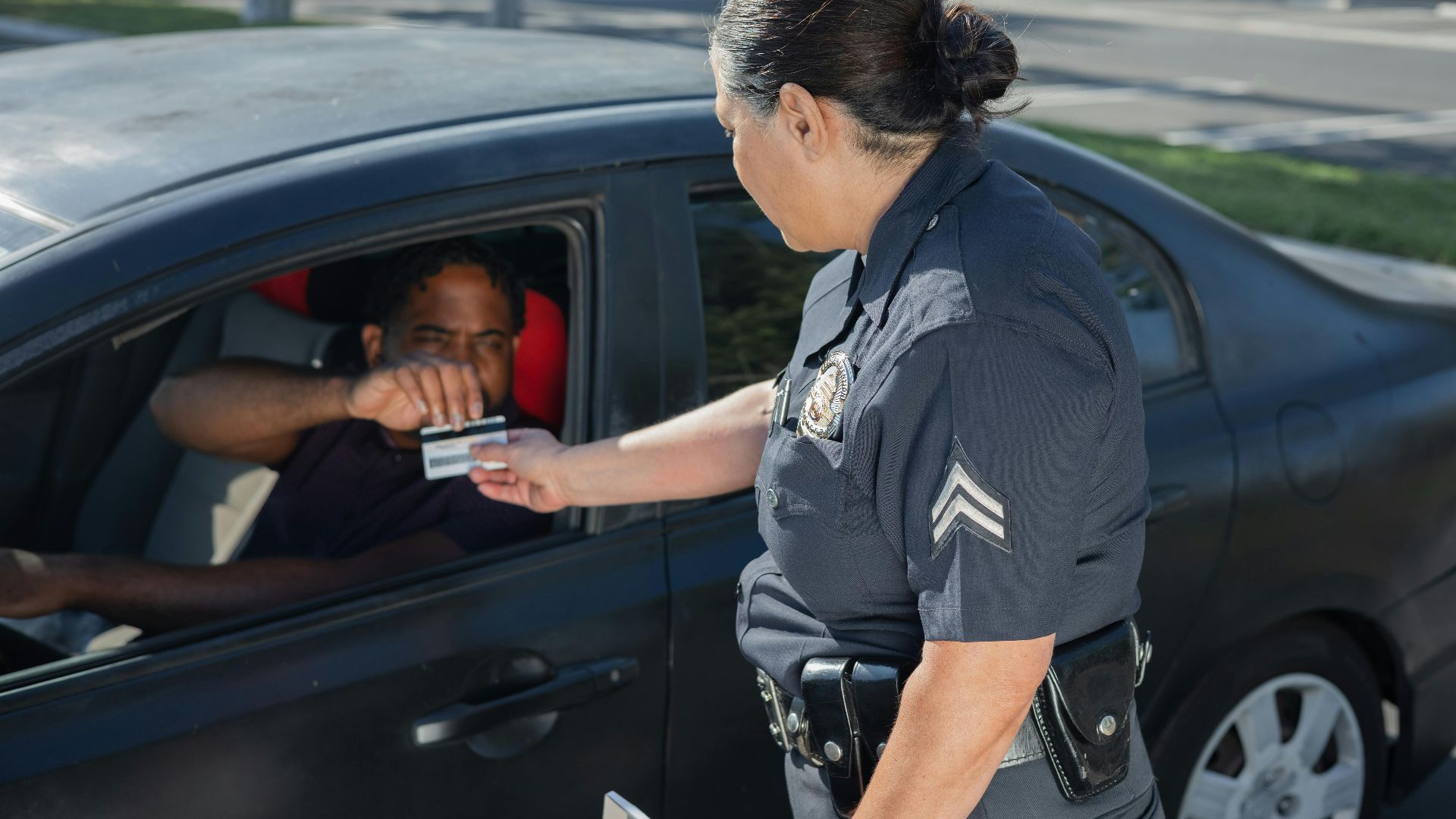 A police officer hands a ticket to a driver in a car on a sunny day street.