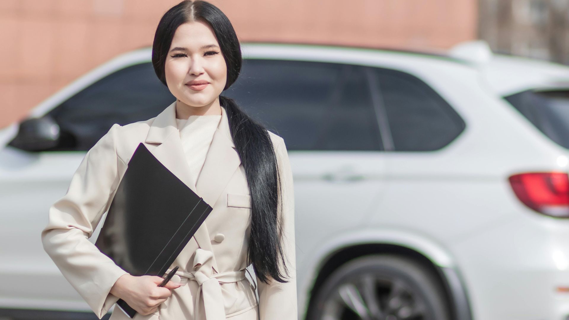 Smiling professional woman standing confidently by a luxury car, embodying success.