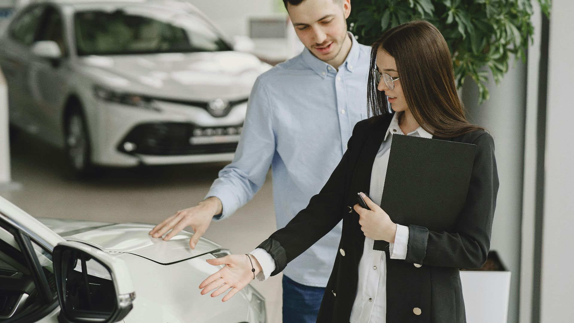 A man and saleswoman discussing a hybrid vehicle's features in an indoor showroom.