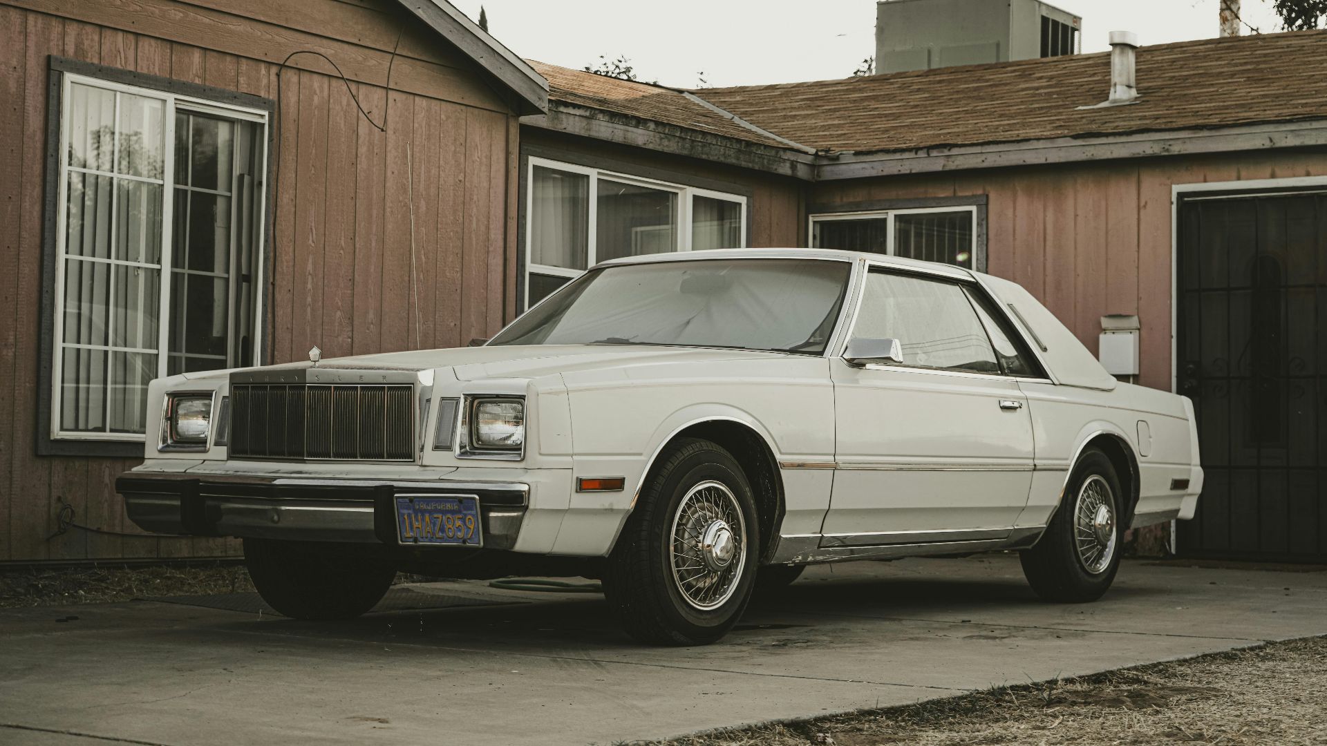 Classic white Chrysler Cordoba parked in front of a retro house with vintage style.