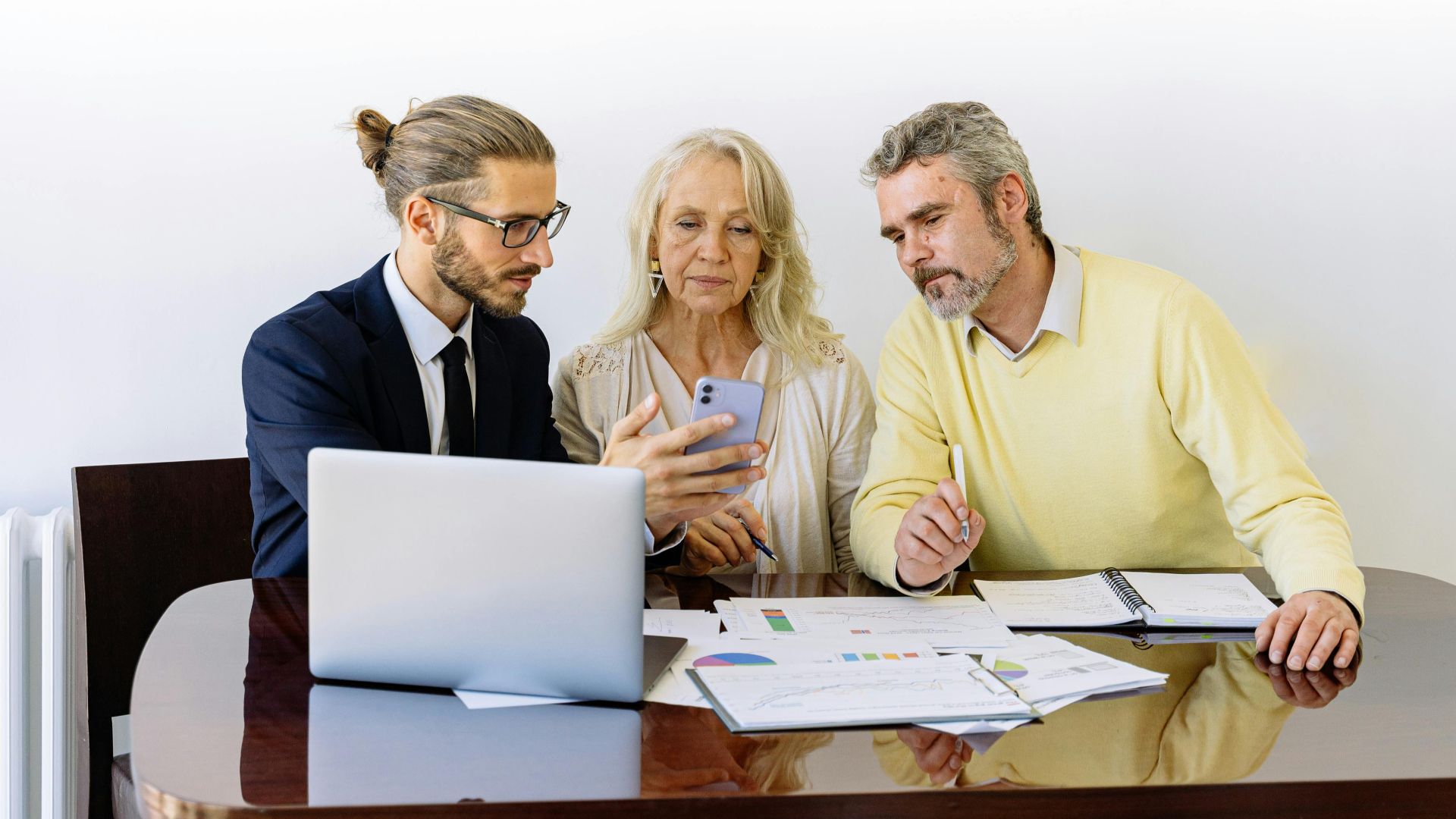 Three individuals collaborating on financial documents during a business meeting.