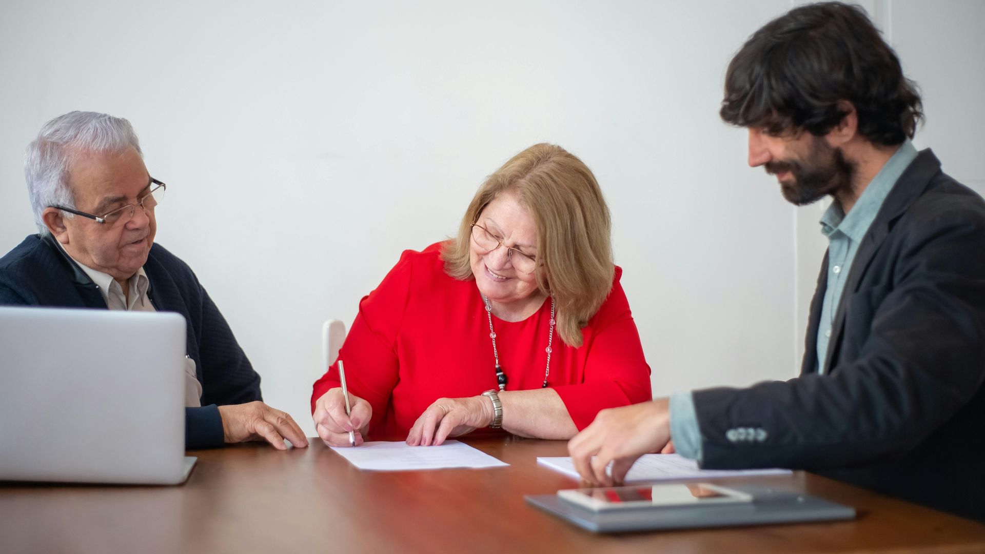 Senior business professionals signing documents during a meeting in a bright office.