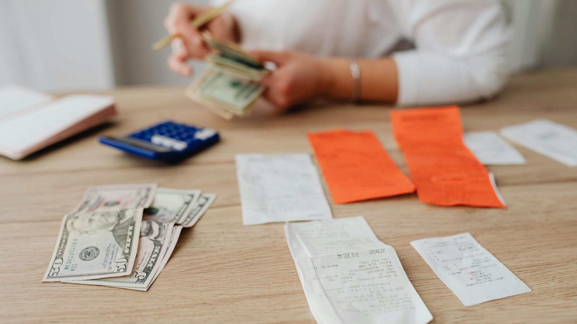 A person using a calculator and cash to plan a household budget.