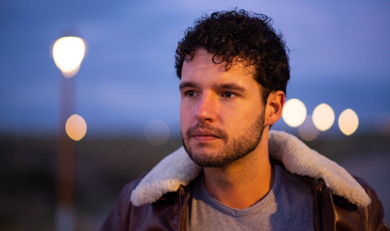 Portrait of a young man with curly hair wearing a leather jacket, captured outdoors at twilight