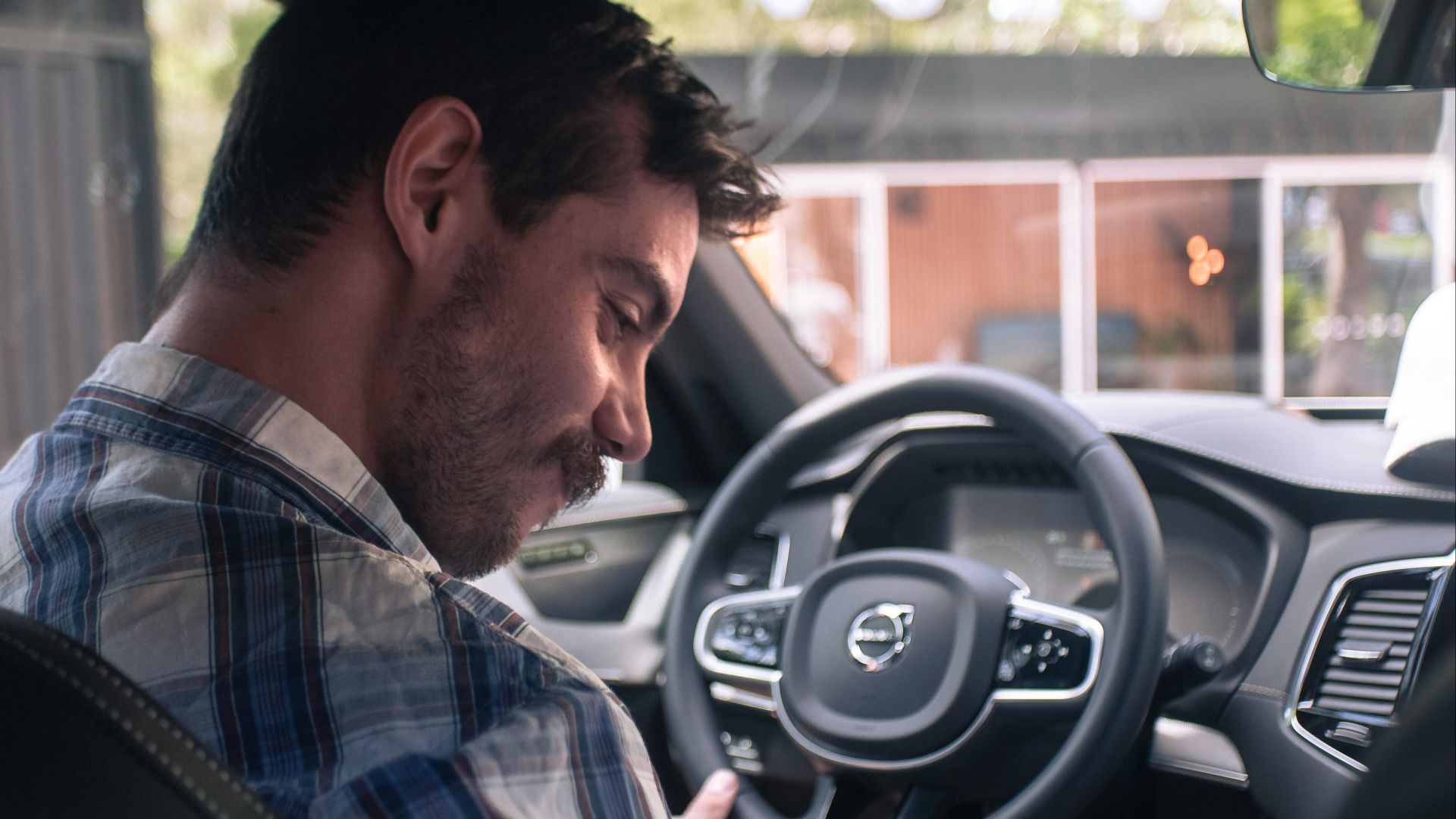 Casually dressed man smiling in the driver seat of a modern Volvo XC90 car interior.
