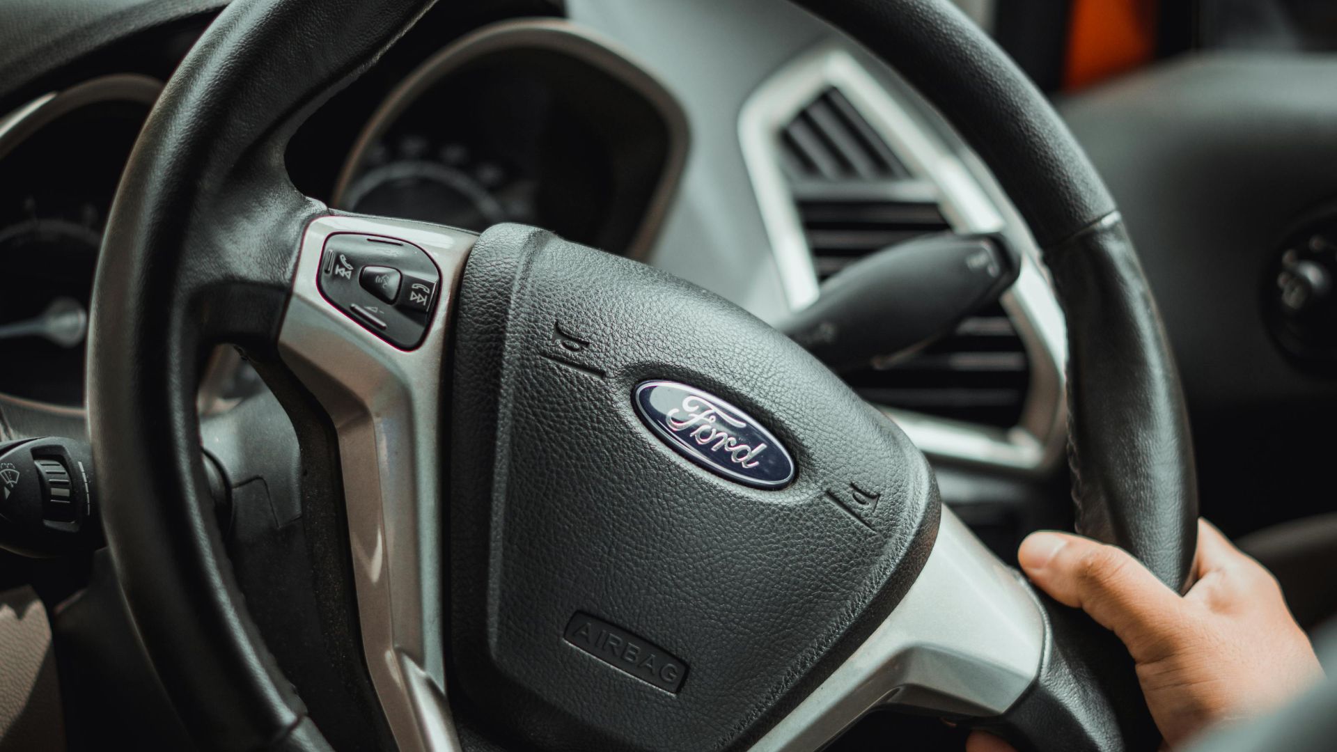 A detailed shot of a hand on a Ford car steering wheel, illustrating automotive interior design.