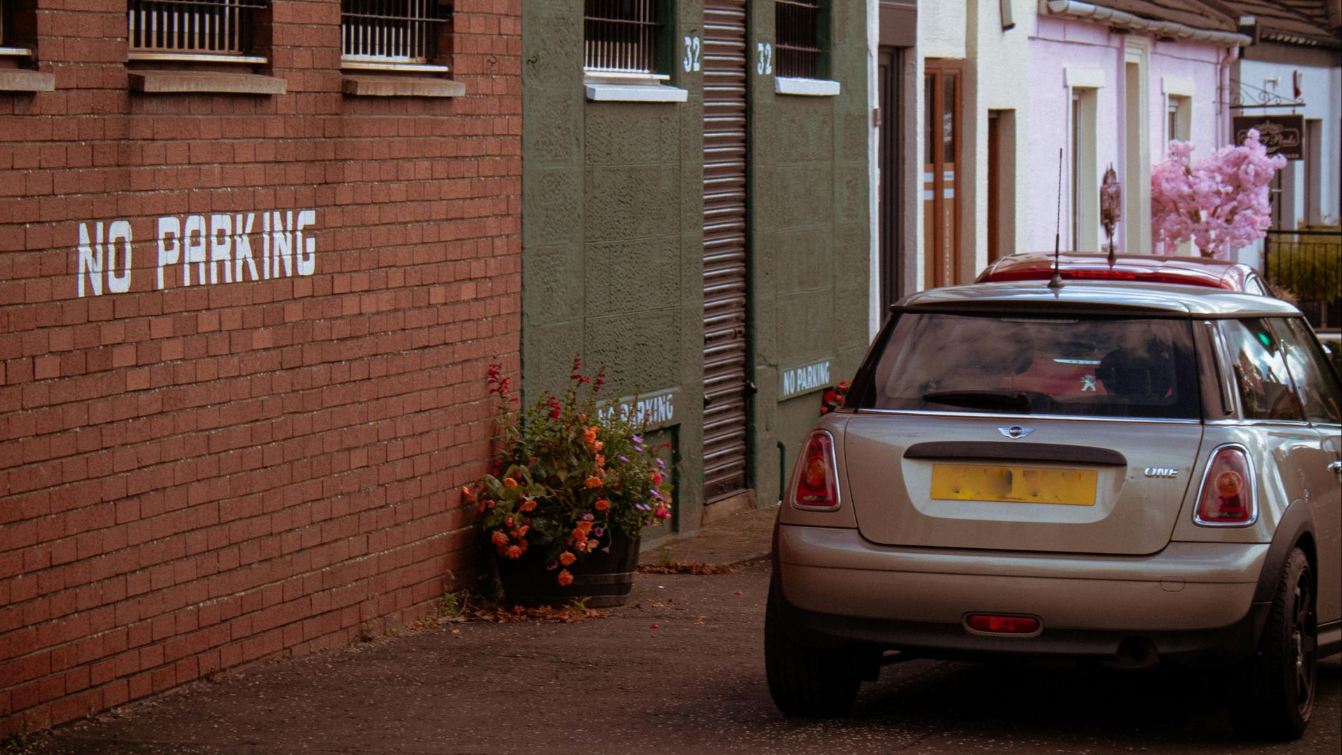 A parked car near a 'No Parking' sign on a charming street with colorful buildings.