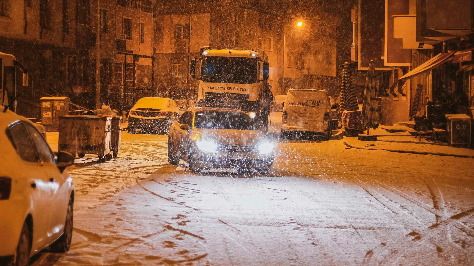 A serene winter night scene of snow-covered street with parked vehicles.