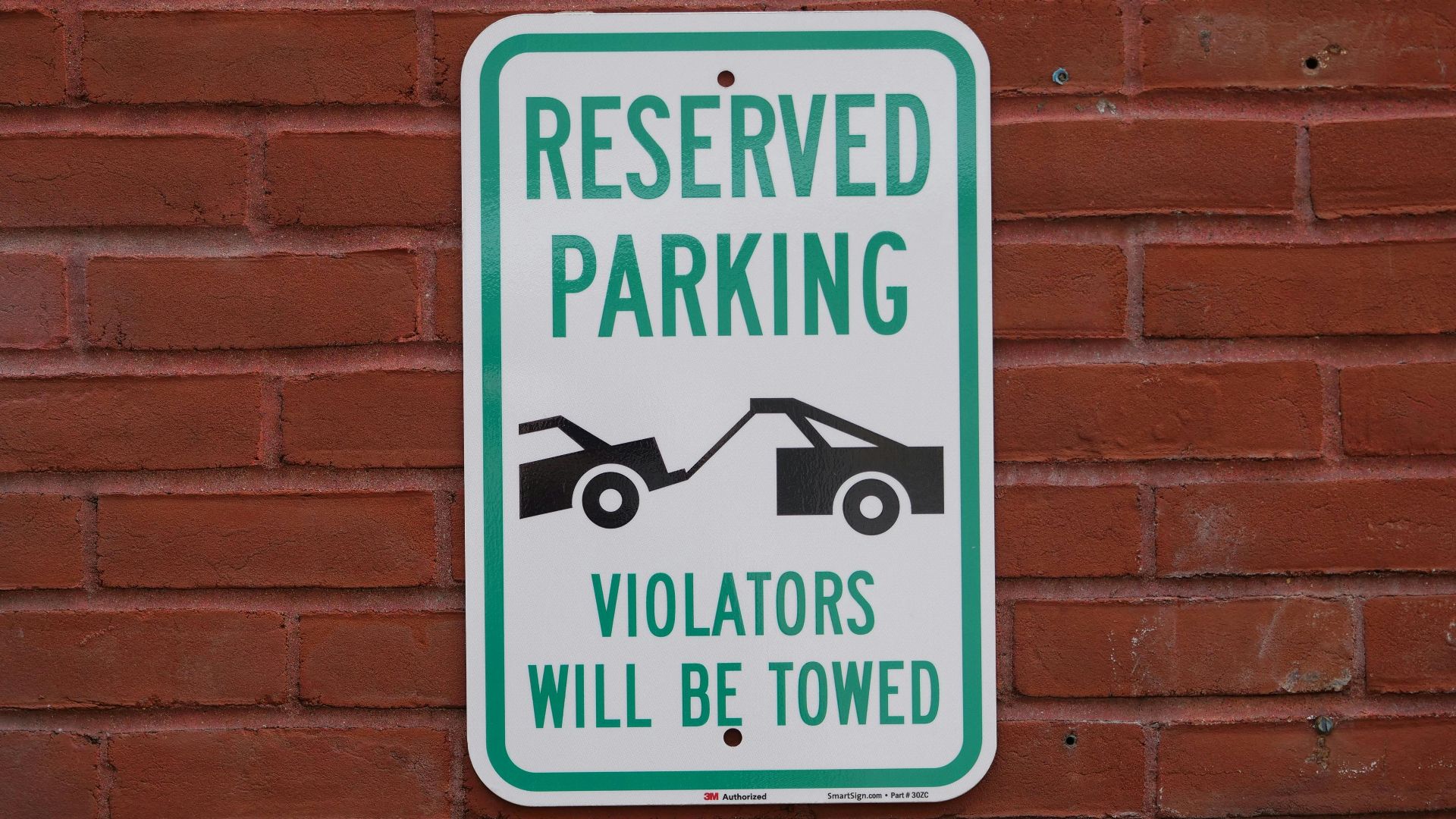 A reserved parking sign on a red brick wall warns that violators will be towed.