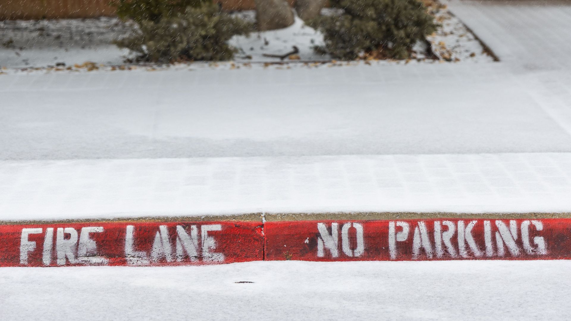Snow-covered urban scene with fire lane no parking sign on sidewalk.