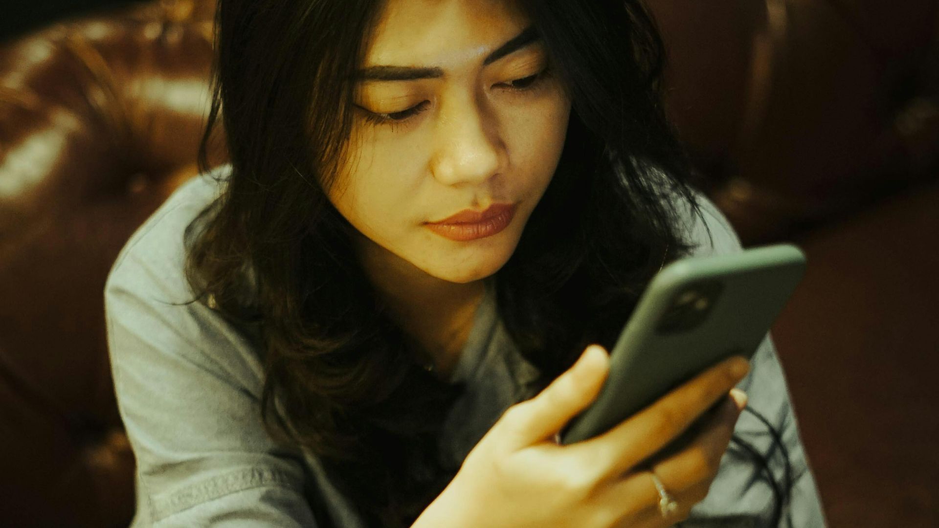 Asian woman sitting with crossed legs on a leather sofa using her mobile phone.