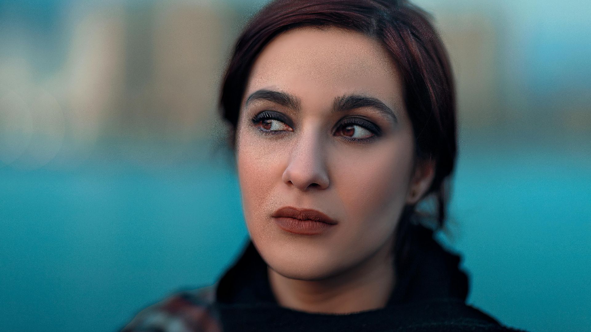 Close-up portrait of a woman with cityscape background and selective focus effect, conveying mood and elegance.