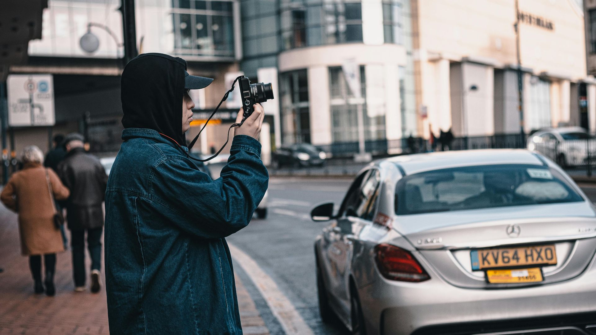 A man taking street photos next to a Mercedes in Birmingham, England.