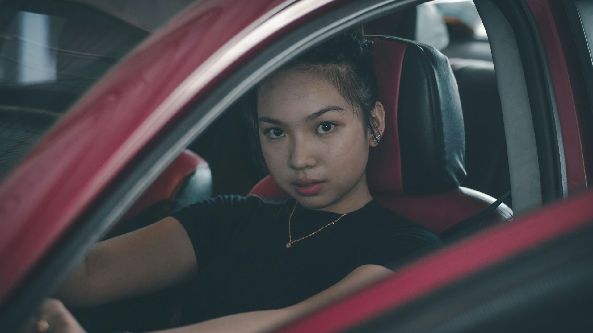 A determined young woman sitting in the driver's seat of a car, ready to drive.
