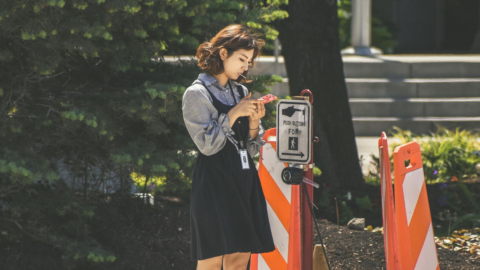 Woman pausing at a pedestrian crossing button in city environment.