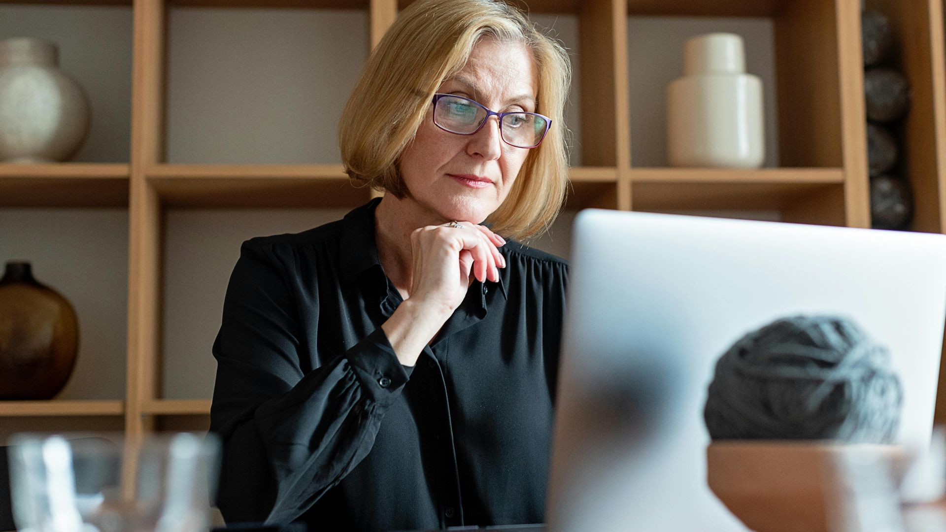 Senior businesswoman with glasses concentrating on work at a home office with a laptop.