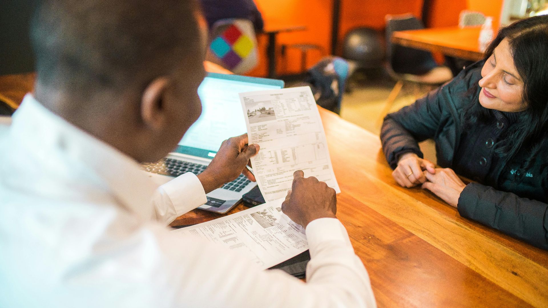 Two adults discussing documents in a business setting indoors.