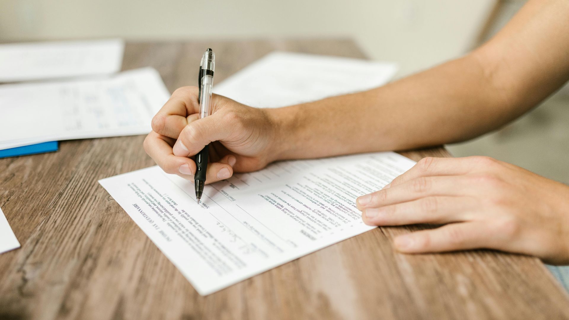Hand filling out paperwork with a pen, showcasing focus on document completion.