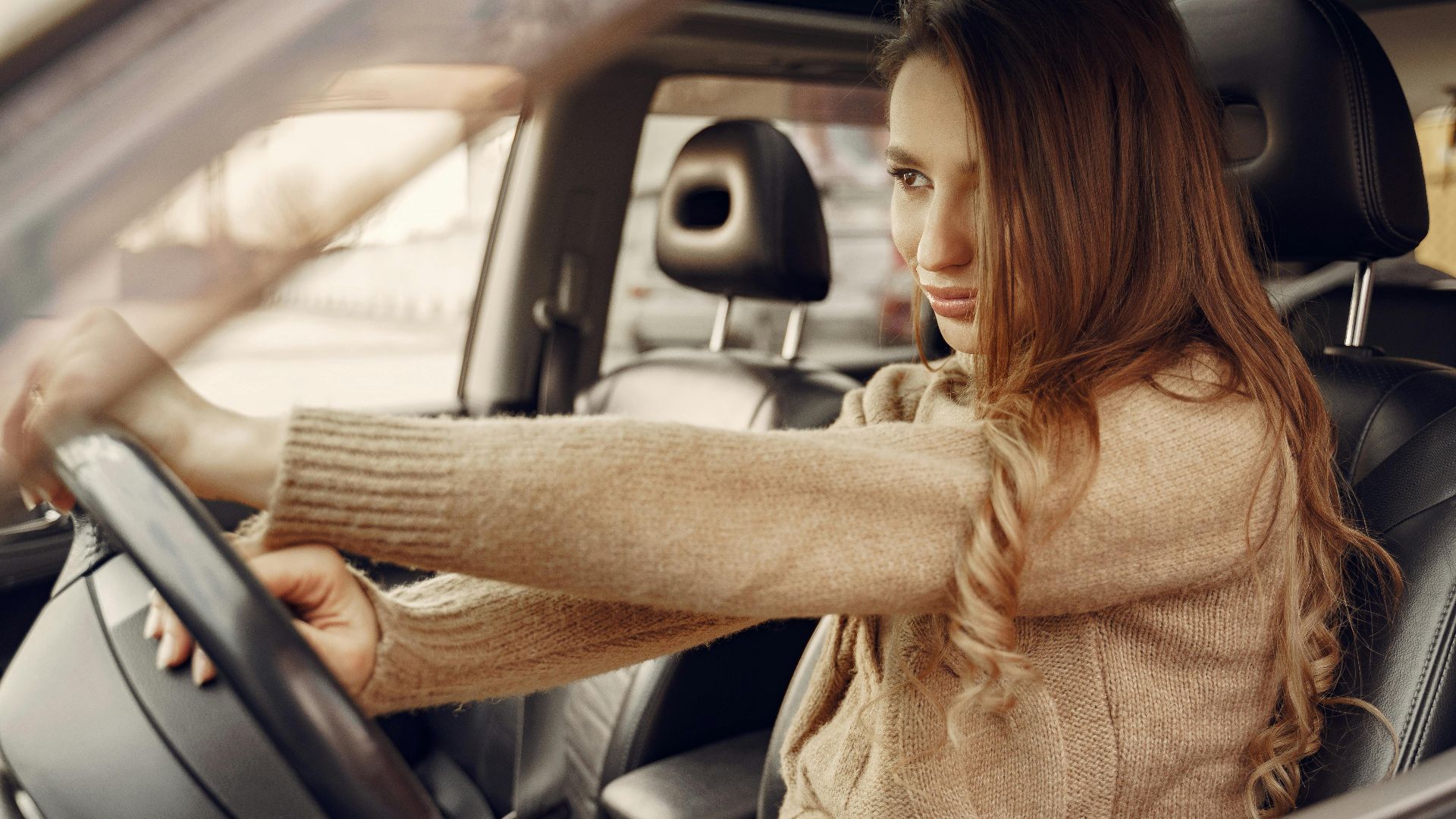 Side view of concentrated contemporary female driver in casual clothes going along street road alone by car with leather interior