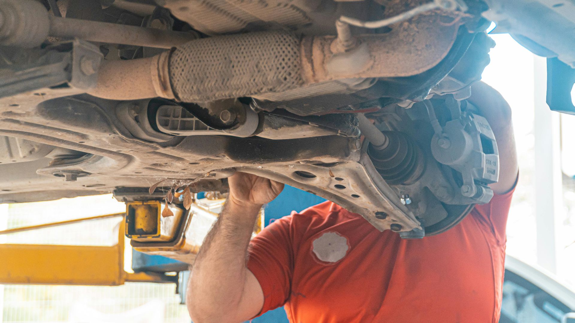 Mechanic working under a vehicle, inspecting the undercarriage in a repair garage, ensuring safety and performance.
