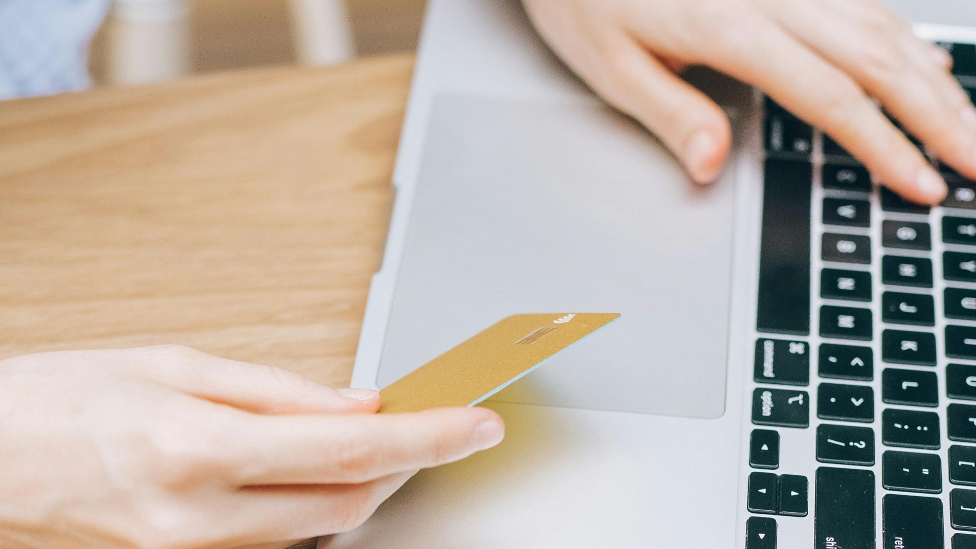 Woman making an online purchase using a credit card and laptop on a wooden table.