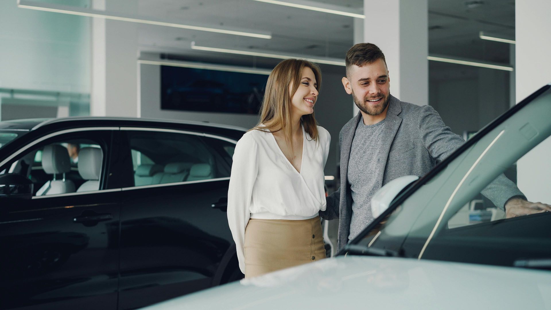 Smiling couple exploring cars at dealership, enjoying shopping experience.