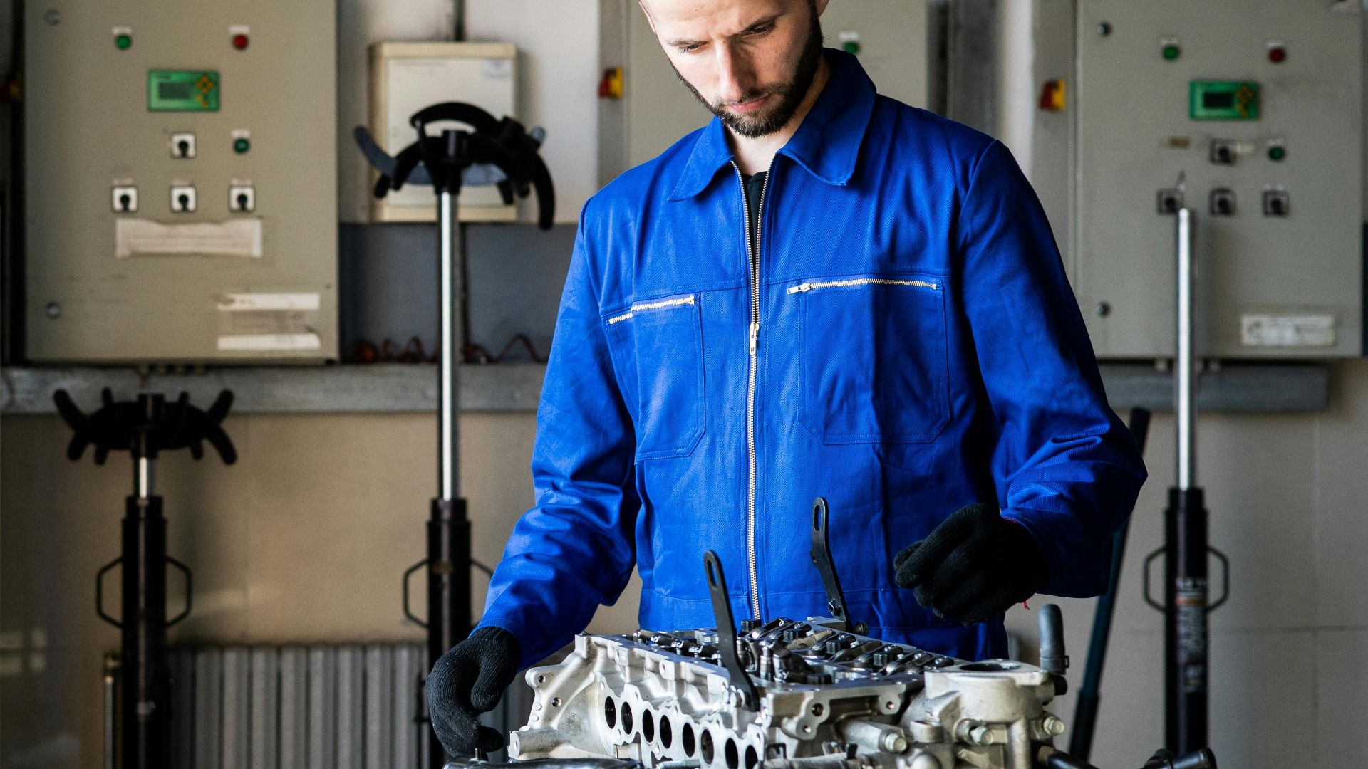 A mechanic in blue coveralls inspects an engine in a repair shop.