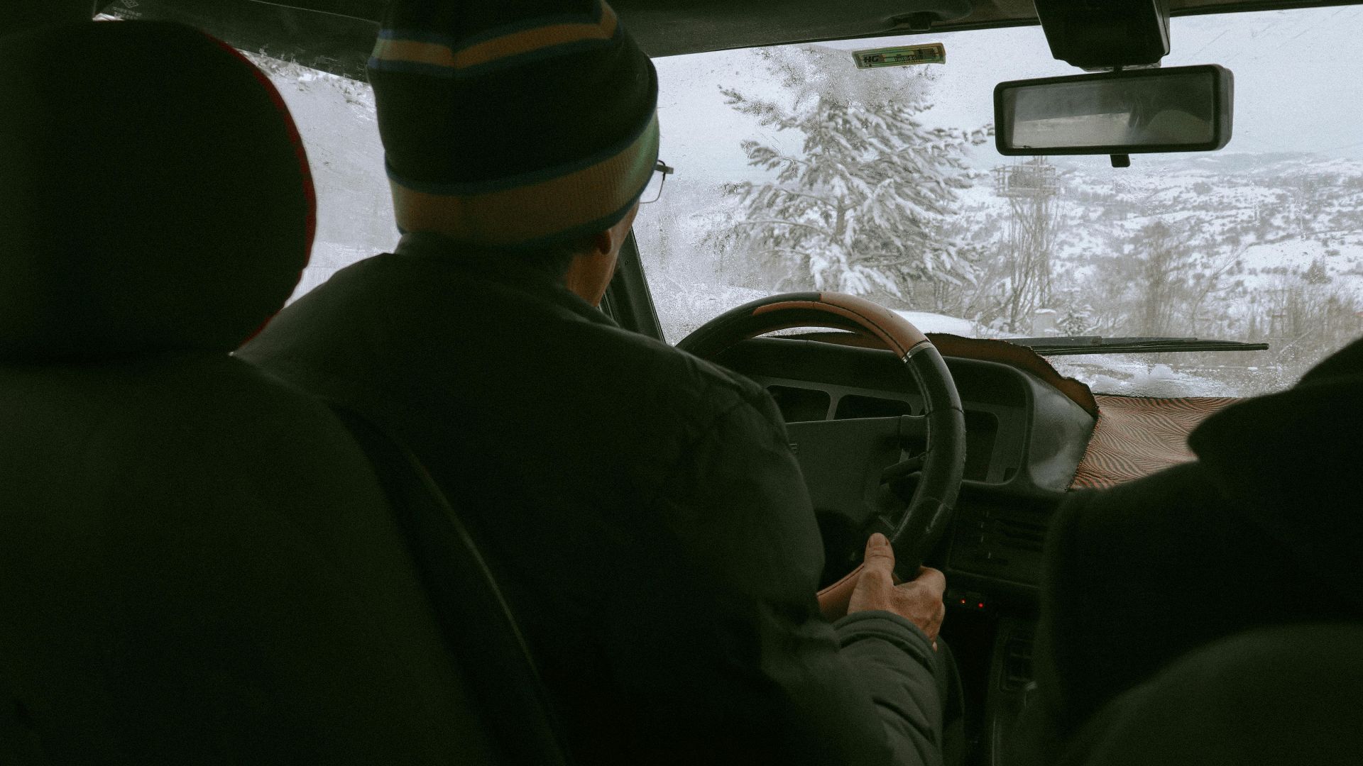 Driver navigating snowy winter landscape from vehicle's interior view.