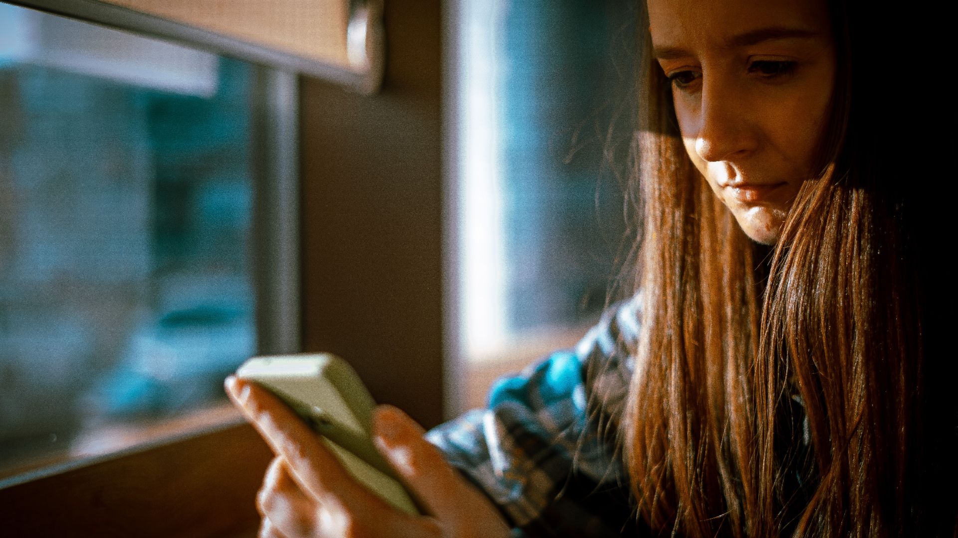 Young woman looking at smartphone with sunlight streaming in through a window.