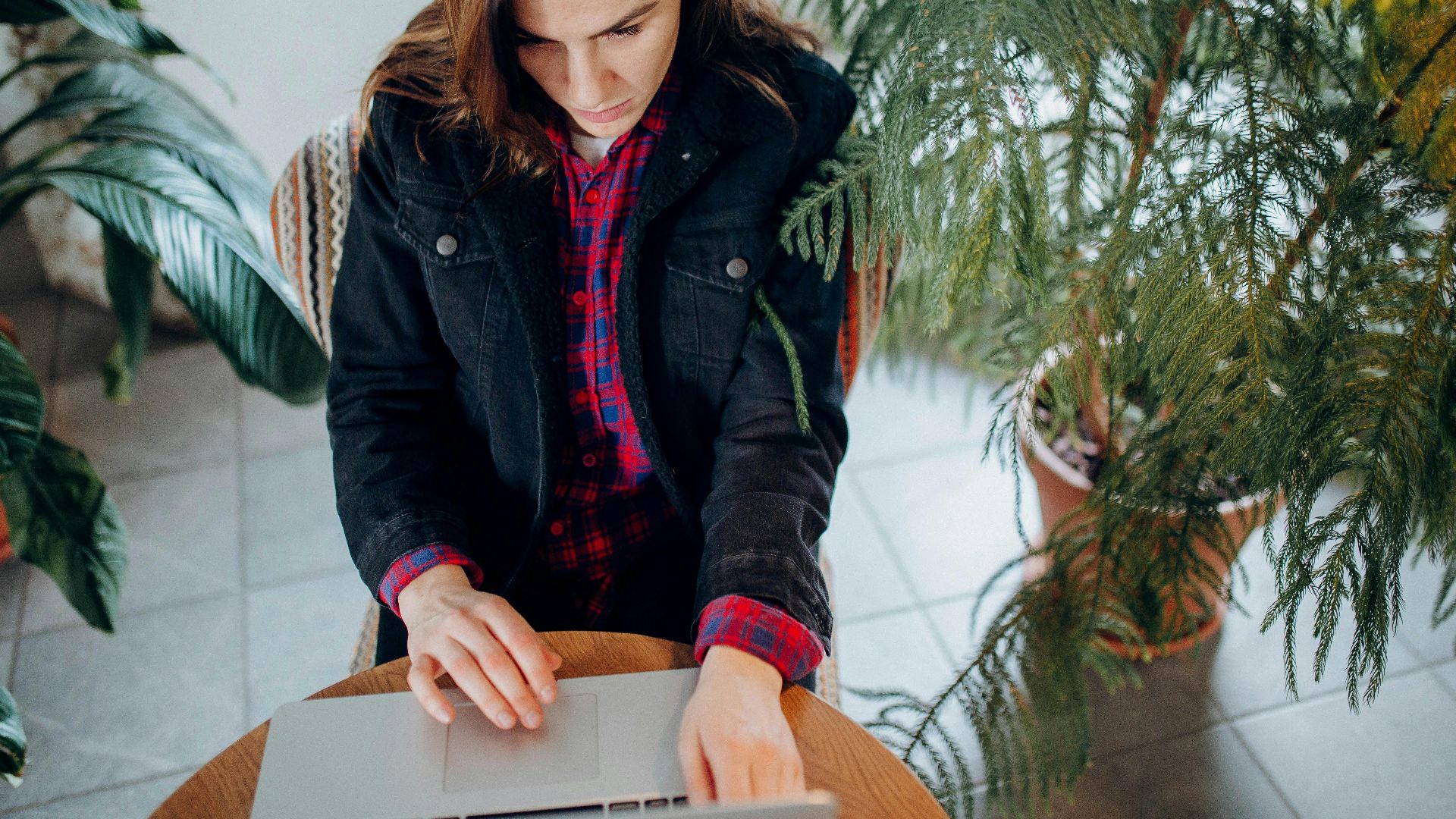 A young woman using a laptop surrounded by plants provides a natural workspace vibe.