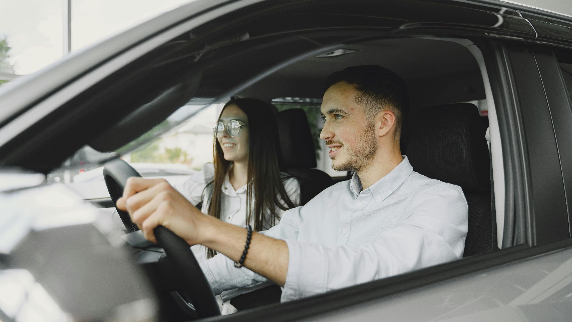 A young couple smiling while driving together in a modern car interior.
