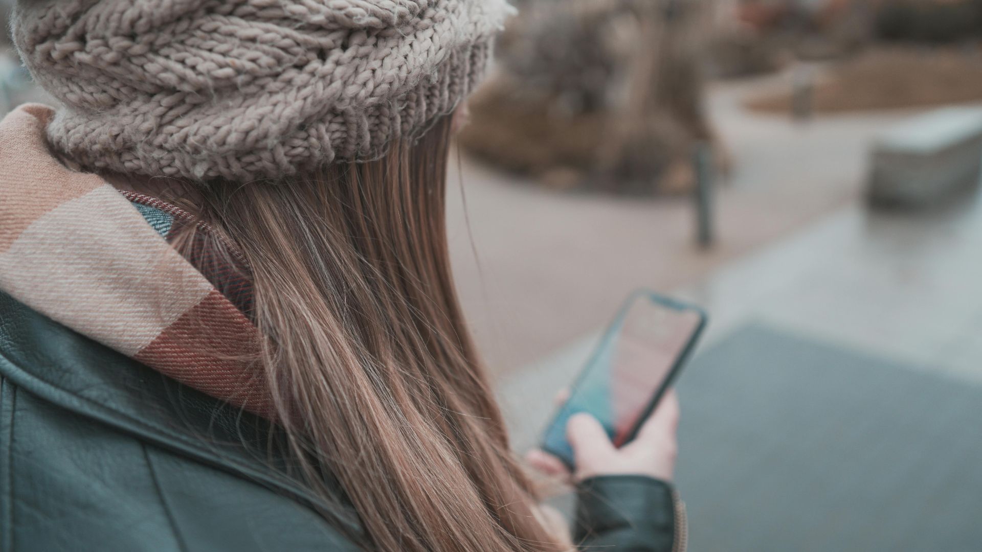A woman wearing a knit cap is texting on her smartphone outdoors in winter.