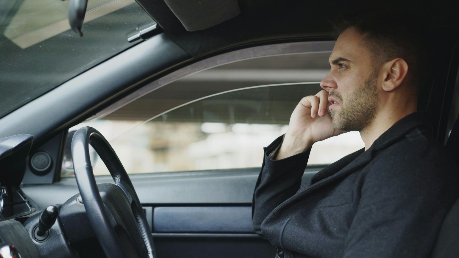 Focused man talking on smartphone in a car during the day, highlighting modern communication.